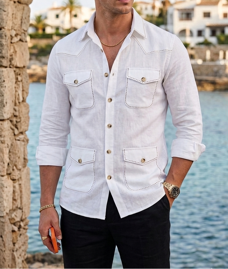 Man wearing a white shirt and sunglasses standing by a stone arch with water and buildings in the background